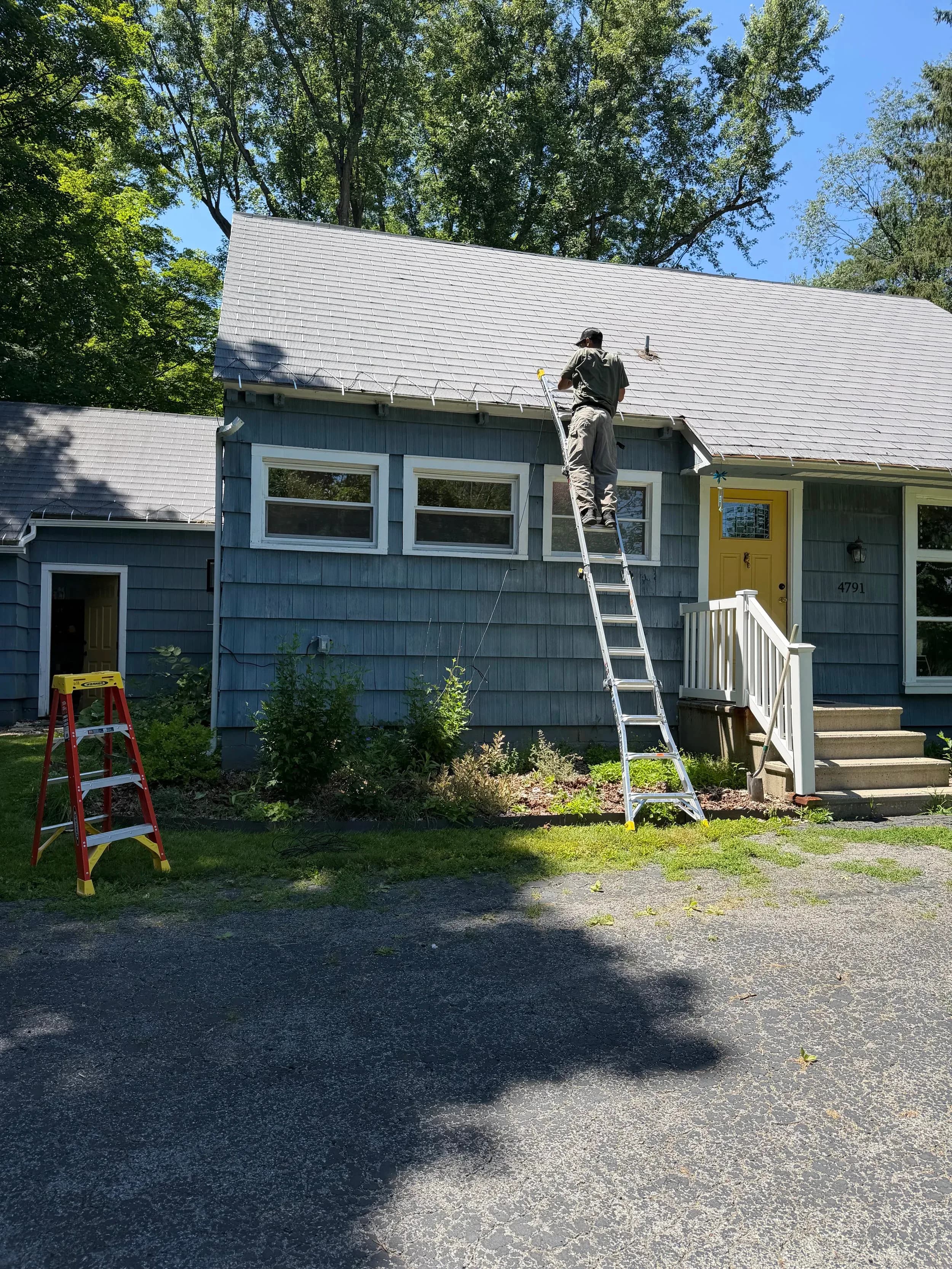 Electrician On Extension Ladder Roofline Lighting Install Second Angle