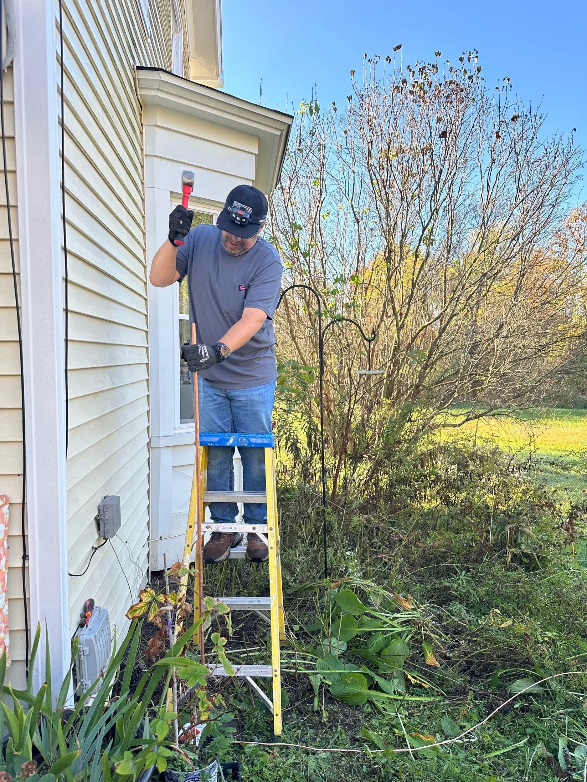 Electrician On Ladder Installing Exterior Outlet