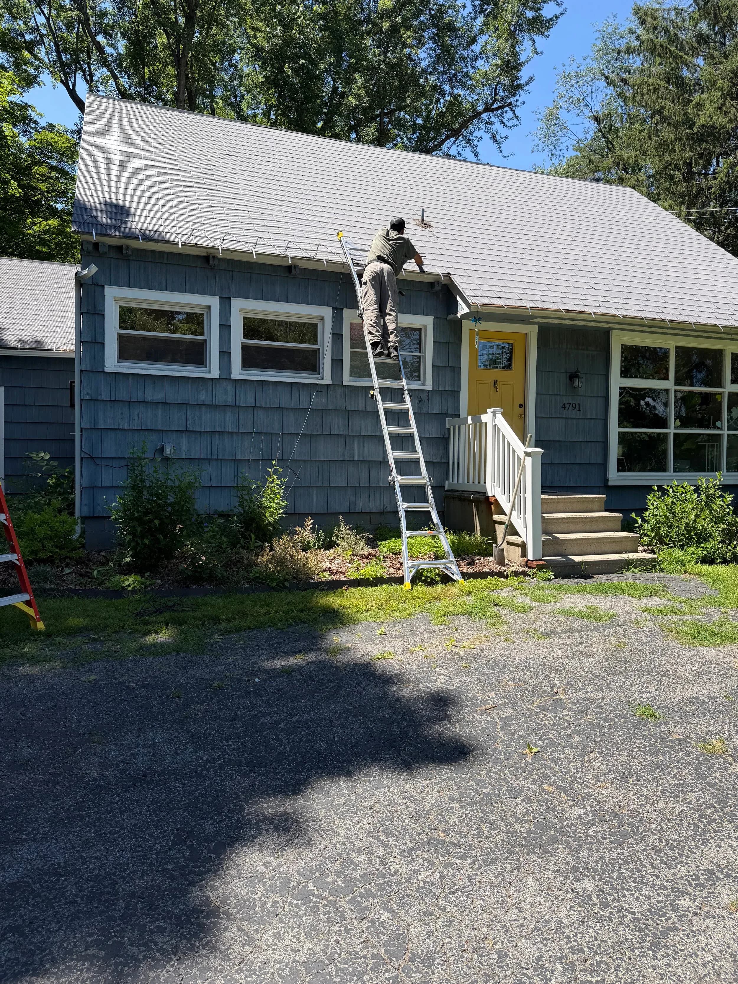 Electrician On Ladder Installing Roofline Lighting Blue House