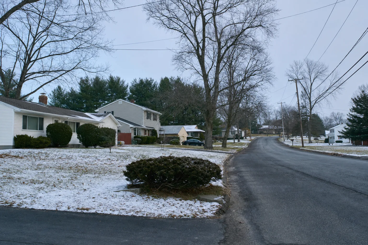 Suburban street of colonial and ranch homes with overhead power lines and light snow in Guilderland, NY