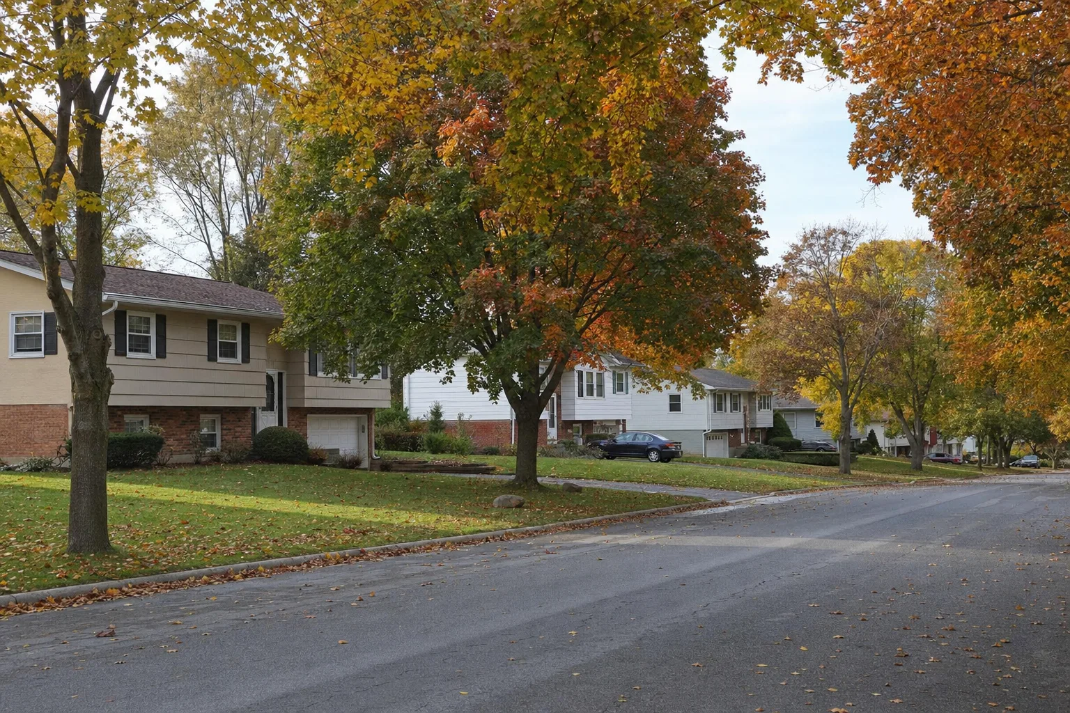 Suburban street of split-level and raised ranch homes with attached garages in Latham, NY in the fall